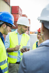 Four people with safety helmets and digital tablet talking at container port - UUF004468