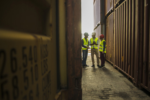 Frau und zwei Männer mit Sicherheitshelmen unterhalten sich im Containerhafen, lizenzfreies Stockfoto