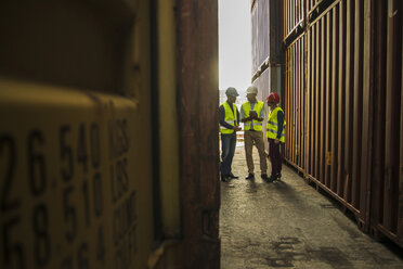 Woman and two men with safety helmets talking at container port - UUF004471