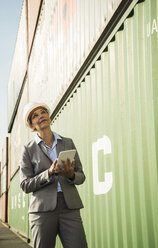 Geschäftsfrau mit digitalem Tablet und Schutzhelm im Containerhafen - UUF004477