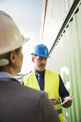 Geschäftsfrau und Mann mit Sicherheitshelmen und digitalem Tablet im Containerhafen - UUF004479