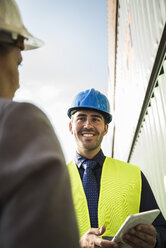 Businesswoman and smiling man with safety helmets at container port - UUF004480