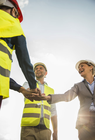 Four happy people with safety helmets stacking their hands outdoors stock photo