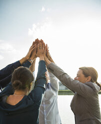 Four happy businesspeople raising their hands together - UUF004483