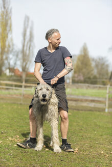 Mann mit seinem irischen Wolfshund auf einer Wiese - TAMF000181