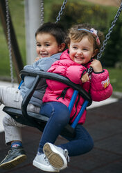 Spain, Little girl and boy sitting laughing on swing - MGOF000245