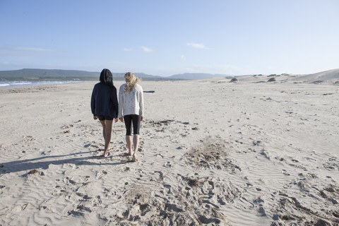 Südafrika, Kapstadt, Rückenansicht von zwei jungen Frauen, die am Strand spazieren gehen, lizenzfreies Stockfoto