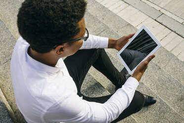 Young man sitting on stairs using a digital tablet - ABZF000063