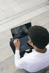 Young man sitting on stairs using a laptop - ABZF000064