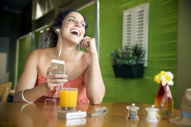 Porträt einer glücklichen Frau, die mit ihrem Smartphone in einem Café Musik hört - TOYF000973