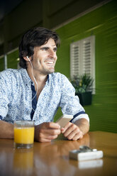 Porträt eines lächelnden Mannes, der mit seinem Smartphone in einem Café Musik hört - TOYF000974