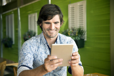Porträt eines lächelnden Mannes, der ein digitales Tablet in einem Café benutzt - TOYF000975
