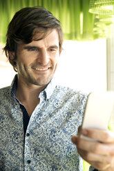 Porträt eines lächelnden Mannes mit Smartphone - TOYF000977