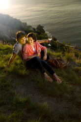 Südafrika, glückliches Paar mit Weißweingläsern, das sich in der Abenddämmerung an der Küste entspannt - TOYF000988