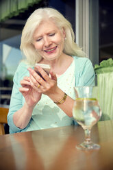 Porträt einer glücklichen älteren Frau, die in einem Café sitzt und ihr Smartphone benutzt - TOYF000996