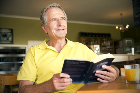 Porträt eines glücklichen älteren Mannes, der mit einem Buch in einem Café sitzt, lizenzfreies Stockfoto