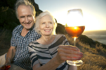 South Africa, happy senior couple with glasses of red wine by sunset - TOYF001003
