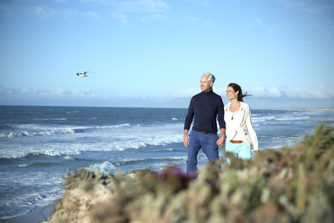 Südafrika, Paar geht Hand in Hand an der Küste entlang, lizenzfreies Stockfoto