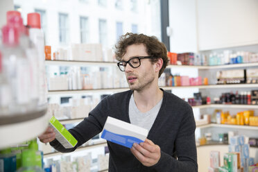 Mann vergleicht Produkte in einer Apotheke - FKF001074