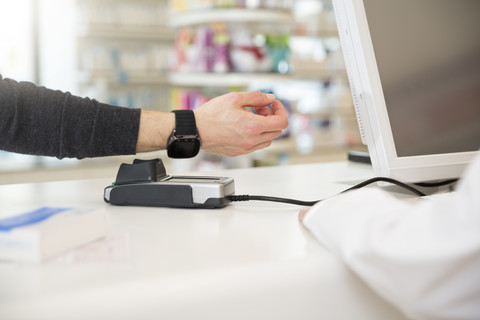 Kunde zahlt bargeldlos mit Smartwatch in einer Apotheke, lizenzfreies Stockfoto