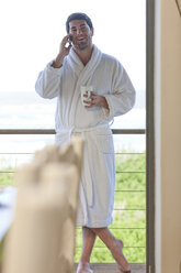 Junger Mann im Bademantel, der in einem Strandhaus mit einem Handy telefoniert - ZEF005345