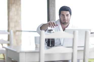 Junger Mann mit Kaffeekanne und Laptop - ZEF005357