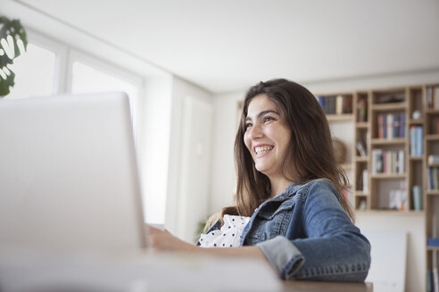 Lächelnde junge Frau mit Laptop zu Hause - RBF002899