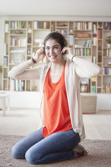 Junge Frau, die zu Hause mit Kopfhörern Musik hört - RBF002874