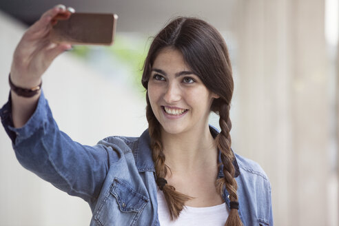 Junge Frau mit Zöpfen macht ein Selfie mit Smartphone - RBF002883