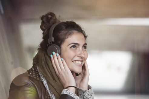 Porträt einer lächelnden jungen Frau, die mit Kopfhörern Musik hört - RBF002892
