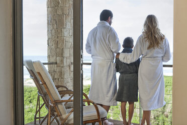 Family in bathrobes standing on patio of beach house - ZEF005395