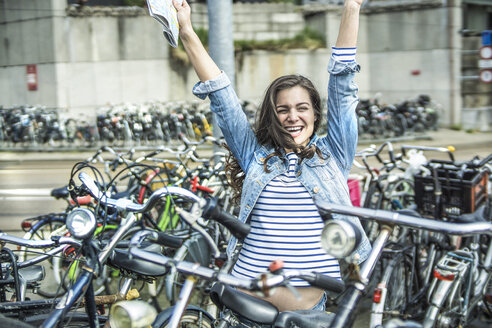 Niederlande, Amsterdam, jubelnde Frau mit Stadtplan zwischen Fahrrädern - RIBF000070