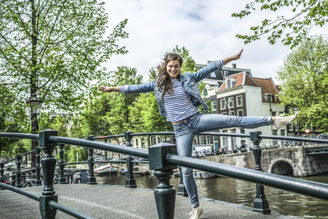 Niederlande, Amsterdam, Touristin balanciert auf einem Bein auf einer Fußgängerbrücke, lizenzfreies Stockfoto