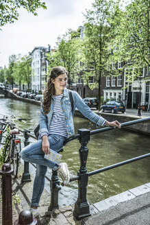 Niederlande, Amsterdam, weibliche Touristin mit Stadtplan vor einem Stadtkanal - RIBF000079