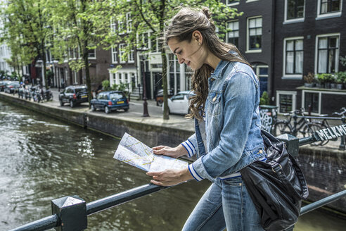 Niederlande, Amsterdam, weibliche Touristin betrachtet Stadtplan vor Stadtkanal - RIBF000085