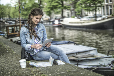 Netherlands, Amsterdam, female tourist using digital tablet in front of town canal - RIBF000088