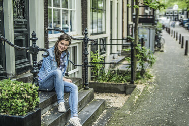 Niederlande, Amsterdam, lächelnde Frau sitzt auf den Stufen vor einem Haus - RIBF000113