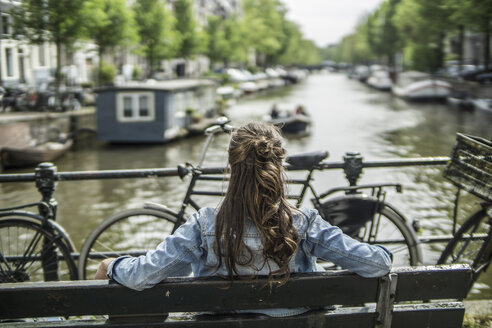 Niederlande, Amsterdam, Frau, die sich auf einer Bank vor einem Stadtkanal räkelt - RIBF000098