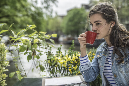 Niederlande, Amsterdam, Frau trinkt eine Tasse Kaffee in einem Straßencafé - RIBF000100