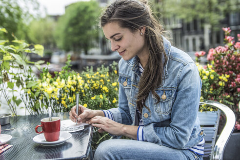 Netherlands, Amsterdam, woman writing postcards in a street cafe - RIBF000101