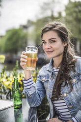 Netherlands, Amsterdam, Portrait of woman drinking glass of beer in a street cafe - RIBF000105