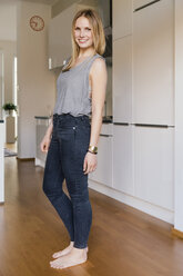 Smiling blond woman standing barefoot in a kitchen - MFF001638