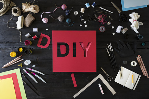 Craft materials, tools and red cardboard with the word DIY on black wood stock photo