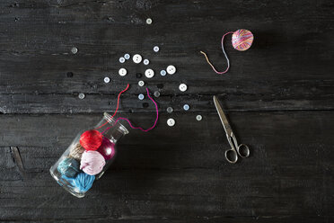 Glass of balls of wool, scissors and buttons on black wood - PDF000947