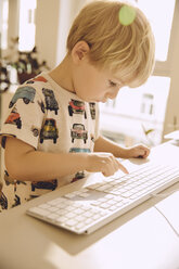 Blond little boy typing on the keyboard of a computer - MFF001643