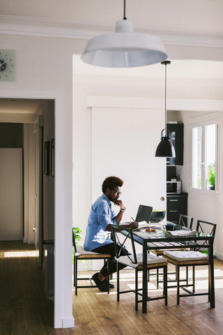 Junger Mann arbeitet mit Laptop im Home Office, lizenzfreies Stockfoto