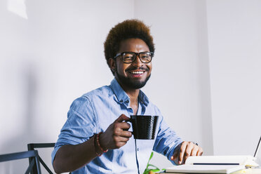 Smiling young man at home office having a coffee break - EBSF000637