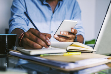 Mann im Büro zu Hause, der sein Smartphone hält und eine Notiz macht - EBSF000642