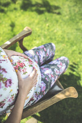 Schwangere Frau sitzt auf einem Holzstuhl in einem Garten - DEGF000421
