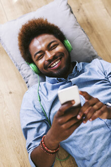 Junger afroamerikanischer Mann mit Kopfhörern und Smartphone auf dem Boden liegend - EBSF000613